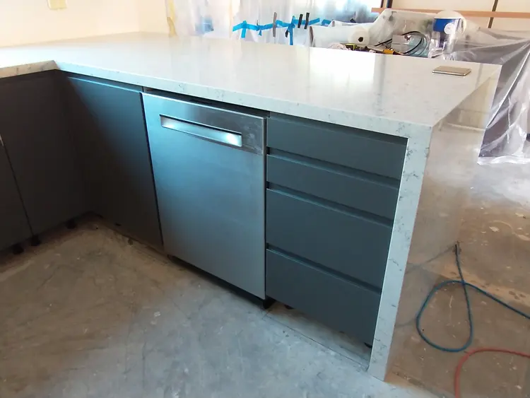 A pale stone benchtop being installed over teal kitchen cabinets
